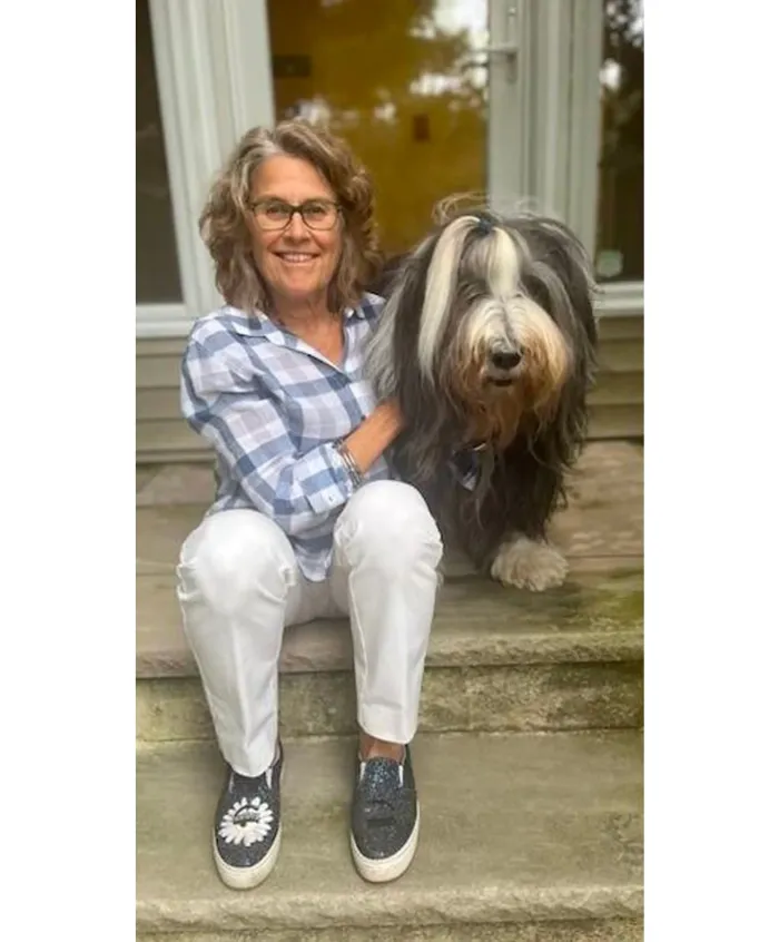 A woman sitting on a porch with a fluffy gray dog